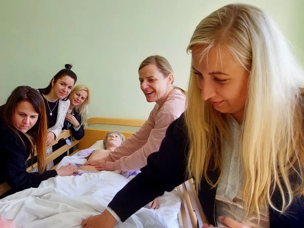 Praktinio mokymo užsiėmimo dalyvės prie slaugos manekeno